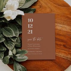 a wedding save the date card on top of a wooden table with flowers and greenery