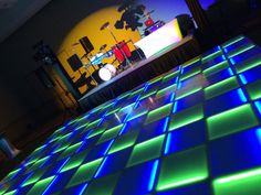 a dance floor that is lit up with blue and green lights in front of a stage