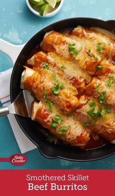 a skillet filled with meat burritos and sauce on top of a blue table