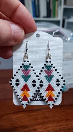 a pair of earrings is being held in front of a book shelf with books on it