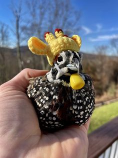 a hand holding a small toy bird with a hat on top of it's head