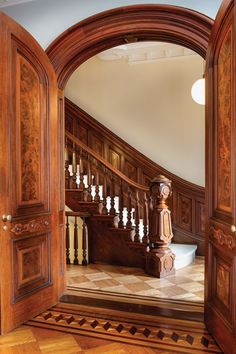 an open door leading to a staircase in a house with wood paneling and handrails