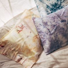 three pillows that have been dyed with different colors and patterns on them sitting on a bed