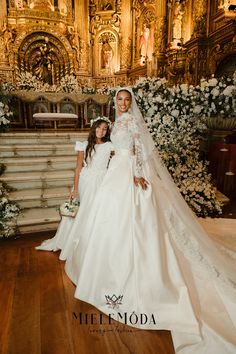 two women in wedding gowns standing next to each other on a wooden floor with white flowers