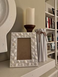 a white photo frame sitting on top of a table next to a candle and some books