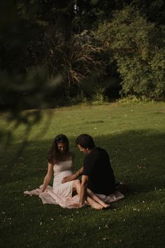 two people sitting on the grass in front of trees