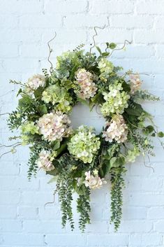 a wreath made out of flowers and greenery hangs on a brick wall in front of a white brick wall