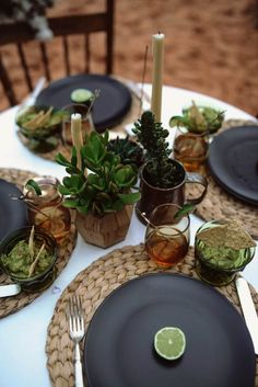 the table is set with black plates, silverware and succulents