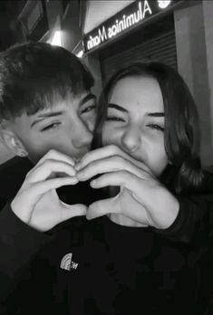 two people are posing for the camera with their hands in the shape of a heart