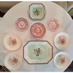 a white table topped with lots of plates covered in red and pink flowers on it