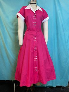 "1950s W:32 Dark Pink Magenta cotton fit and flare white pique collared short sleeve button up dress with pockets! Vintage 50s beautiful fit and flare dress. Made out of solid dark pink/magenta cotton with cotton pique white contrast. Bodice darted, with cuffed sleeves and collared neckline. Rows of 3 plastic buttons that looks like a small toothpaste caps. One of a kind. Unlined. Added petticoat not included.  MEASUREMENTS  Bust: 40\" Waist: 32\" Hips: free Bodice length: 18\" Skirt length: 30\" with no hem available to let down This is in good vintage condition, overall wear to fabrics due age, presents beautifully and is completely wearable as is! ✨" Fitted Cotton Short Sleeve Shirt Dress, Fitted Short Sleeve Dresses With Covered Buttons, Fitted Cotton Shirt Dress With Placket, 1950s Style Vintage Short Sleeve Dress For Work, Retro Fitted Shirt Dress With Buttons, Retro Short Sleeve Dress With Buttons, Classic Short Sleeve Dress With Button Cuffs, Cotton Dress With Buttons And Spread Collar, 1950s Style Short Sleeve Day Dresses