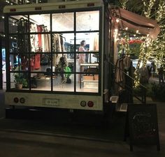 a truck is parked in front of a store with lights on the windows and people standing outside