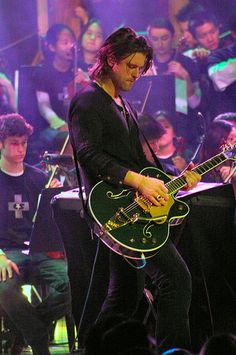 a man playing guitar on stage with other people in the background