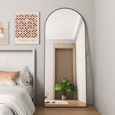 a white bed sitting under a large mirror next to a wooden table with a potted plant on it