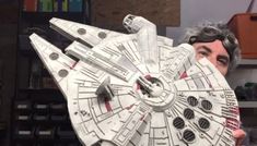 a man holding up a paper model of a star wars millennium falcon in front of his face