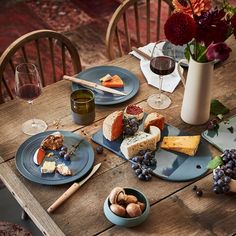 a wooden table topped with blue plates filled with cheese and crackers next to wine glasses