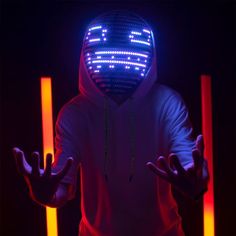 a man in a white hoodie wearing a neon mask and holding his hands up