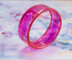 a pink ring sitting on top of a colorful tablecloth covered surface with paint splattered all over it