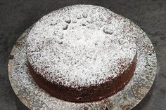 a chocolate cake covered in powdered sugar on top of a white plate with silver trim