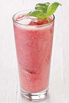 a glass filled with a pink drink on top of a white table next to a green leaf