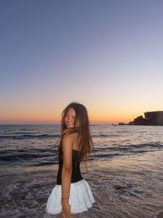 a woman standing in the ocean at sunset