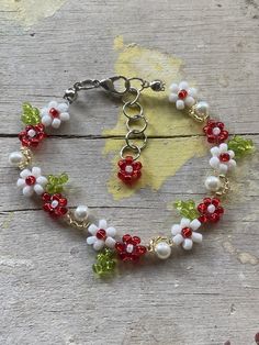 a bracelet with red, white and green beaded flowers sits on a piece of wood