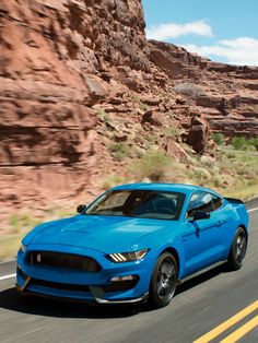 a blue mustang is driving down the road in front of some red rocks and grass