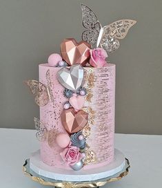 a pink and gold decorated cake on a stand with butterflies, flowers, and jewels