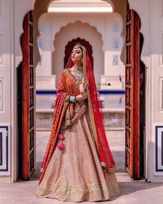 a woman in a red and gold lehenga is posing for the camera with her hand on her hip