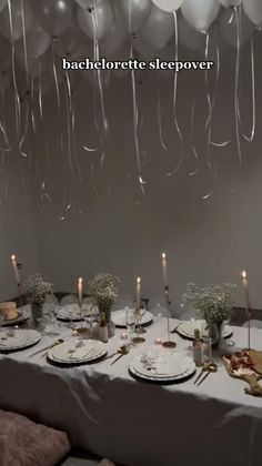 the table is set with white plates and silverware, candles, and balloon garlands