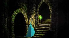 a woman in a blue dress standing at the end of a set of stone stairs