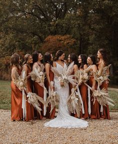 a group of women standing next to each other in front of trees and gravel ground