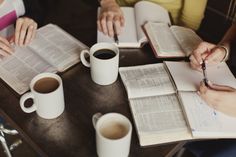 three people sitting at a table with open books and coffee cups in front of them