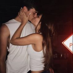 a man and woman kissing in front of a street sign with the light on behind them