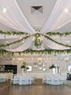 the inside of a banquet hall decorated with greenery and white draping over tables