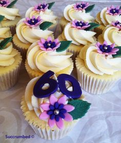 cupcakes decorated with purple and white frosting are arranged on a tablecloth