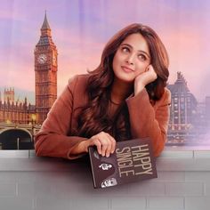 a woman leaning on a wall holding a book in front of her face with the big ben clock tower in the background