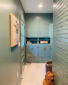 a long narrow hallway with blue cabinets and white tile flooring, along with baskets on the wall