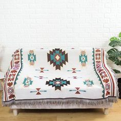 a couch covered in a colorful blanket sitting on top of a wooden floor next to a potted plant