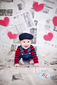 a baby sitting on top of a bed wearing a hat and overalls with hearts flying above it