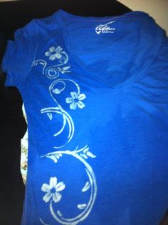 a blue t - shirt with white flowers on it sitting on a black table next to a cell phone