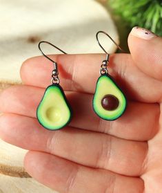 an avocado shaped earrings is being held in someone's hand