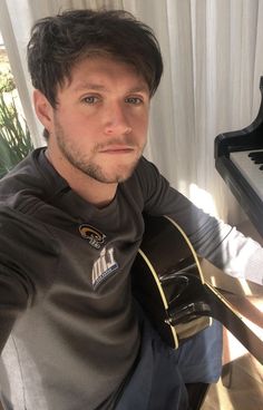 a man sitting at a table with a guitar in his hand and looking into the camera