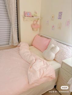 a bed with pink sheets and pillows in a small room next to a white dresser