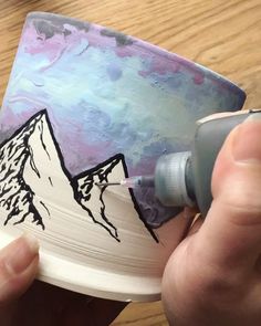 someone is painting a mountain on a paper cup