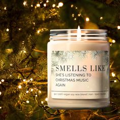 a candle that is sitting in front of a christmas tree with the words smells like she's listening to christmas music again