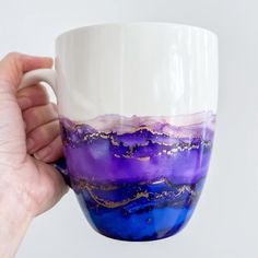 a hand holding a coffee cup with purple and white paint on it's side