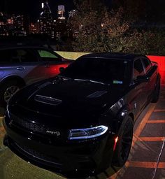 two cars parked next to each other in a parking lot with city lights behind them