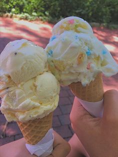 two ice cream cones with sprinkles are held up in front of the camera