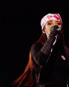 a woman with long red hair wearing a bandana and holding a microphone up to her mouth